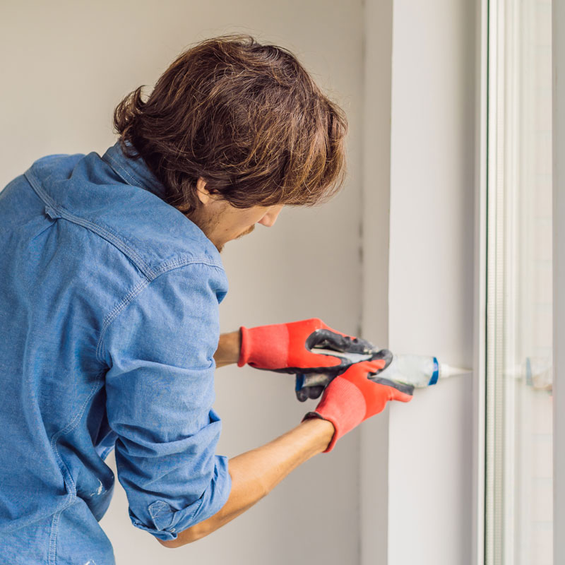 Man in blue shirt caulking around window.